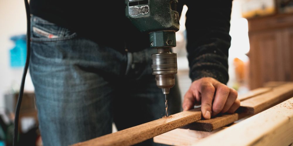 Close-up of a person using an electric drill on a wooden plank, showcasing detailed woodworking skills.