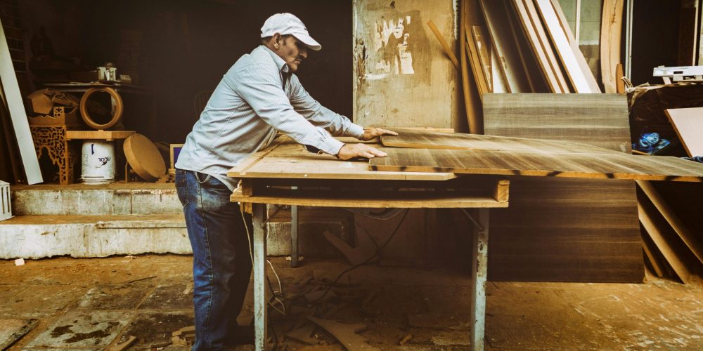 Carpenter focuses on woodworking project inside a busy workshop, surrounded by materials.
