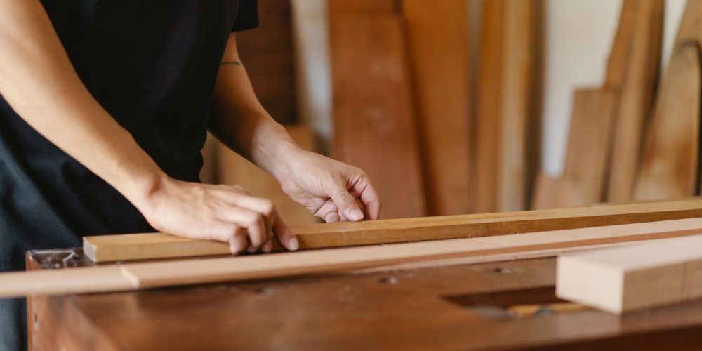 Close-up of a craftsman measuring wood in a workshop, highlighting skill and precision.